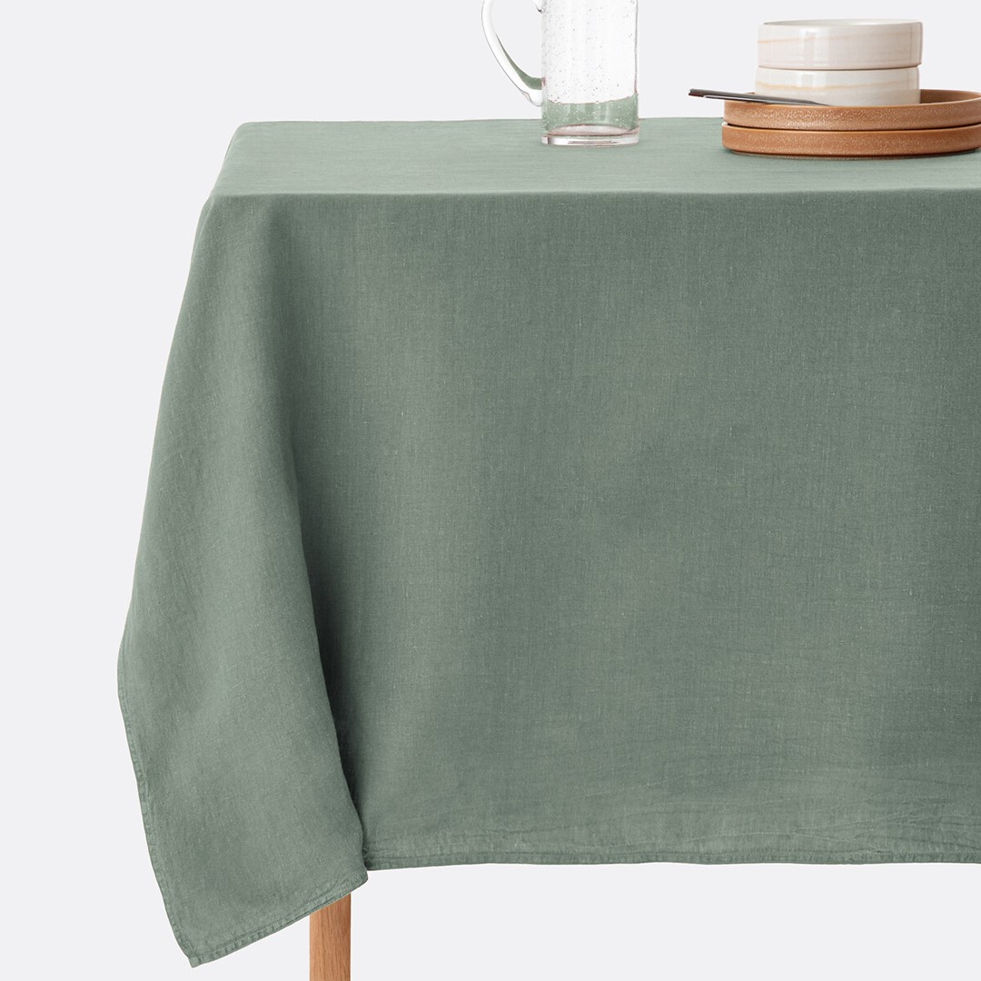 Groen linnen tafelkleed met servies en glazen op een gedekte tafel in een natuurlijke, rustige stijl