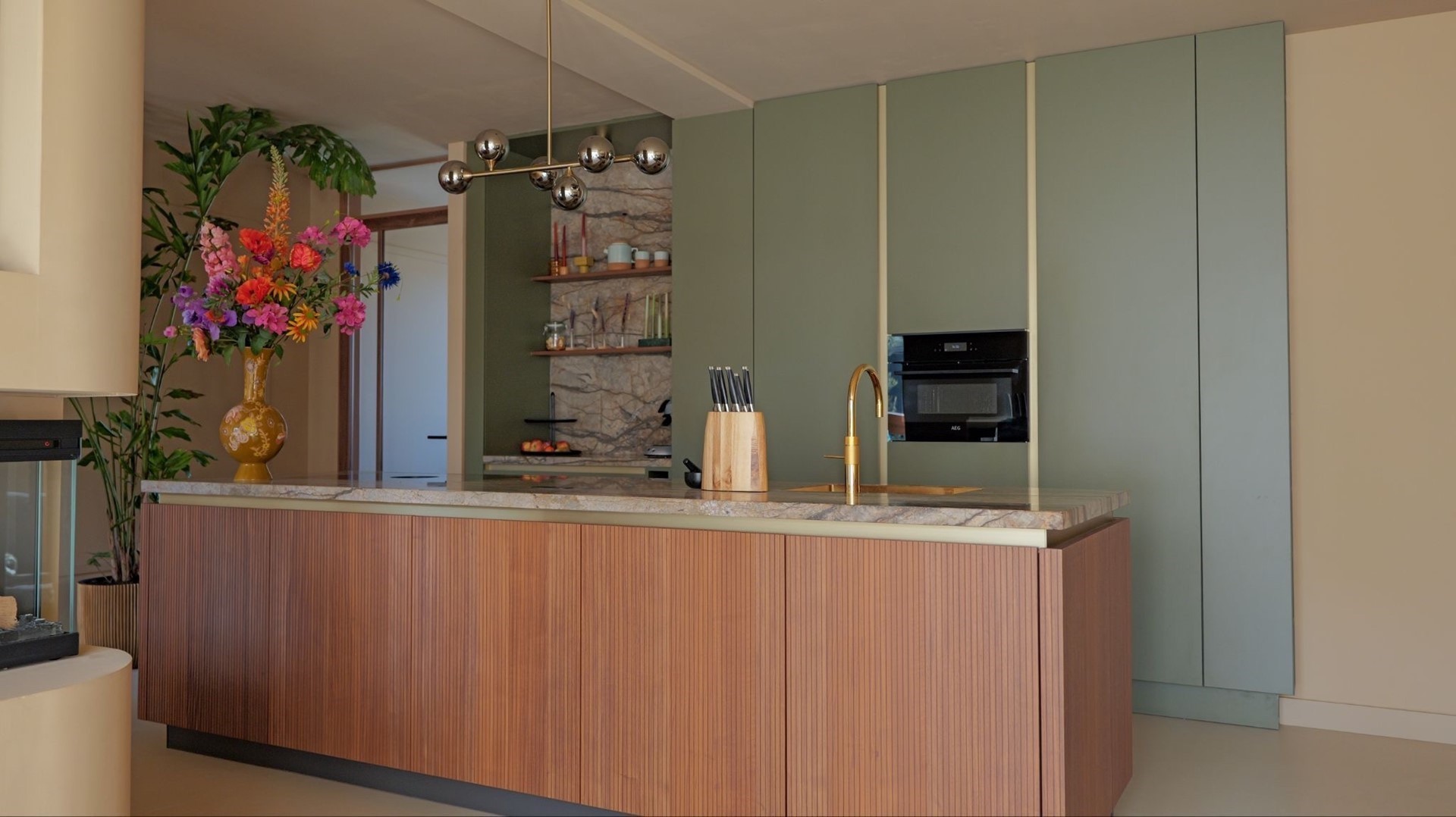 Kookeiland met geribbeld walnoothout front en marmeren werkblad, met olijfgroene kastenwand en gouden kraan op de achtergrond