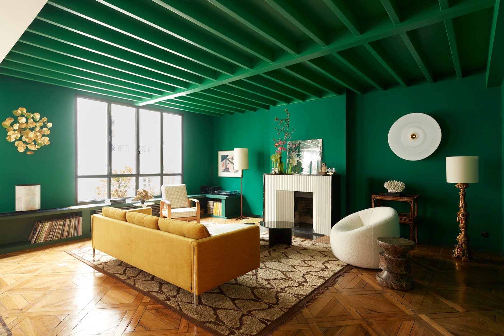 De woonkamer is geschilderd in drie tinten smaragdgroen. Op de vloer ligt een handgeknoopt tapijt uit Marokko van wol en jute. Het stenen krukje voor de Pumpkin Chair van Pierre Paulin is van Le Berre Vevaud chez The Invisible Collection.