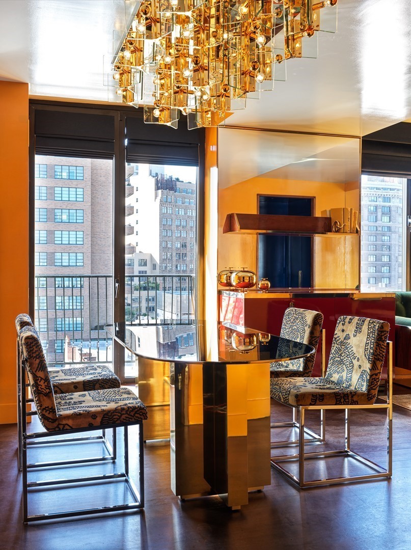 Interieur van een suite in The Manner New York met messing kroonluchter, spiegelwand, glanzend rood meubel en uitzicht op SoHo.