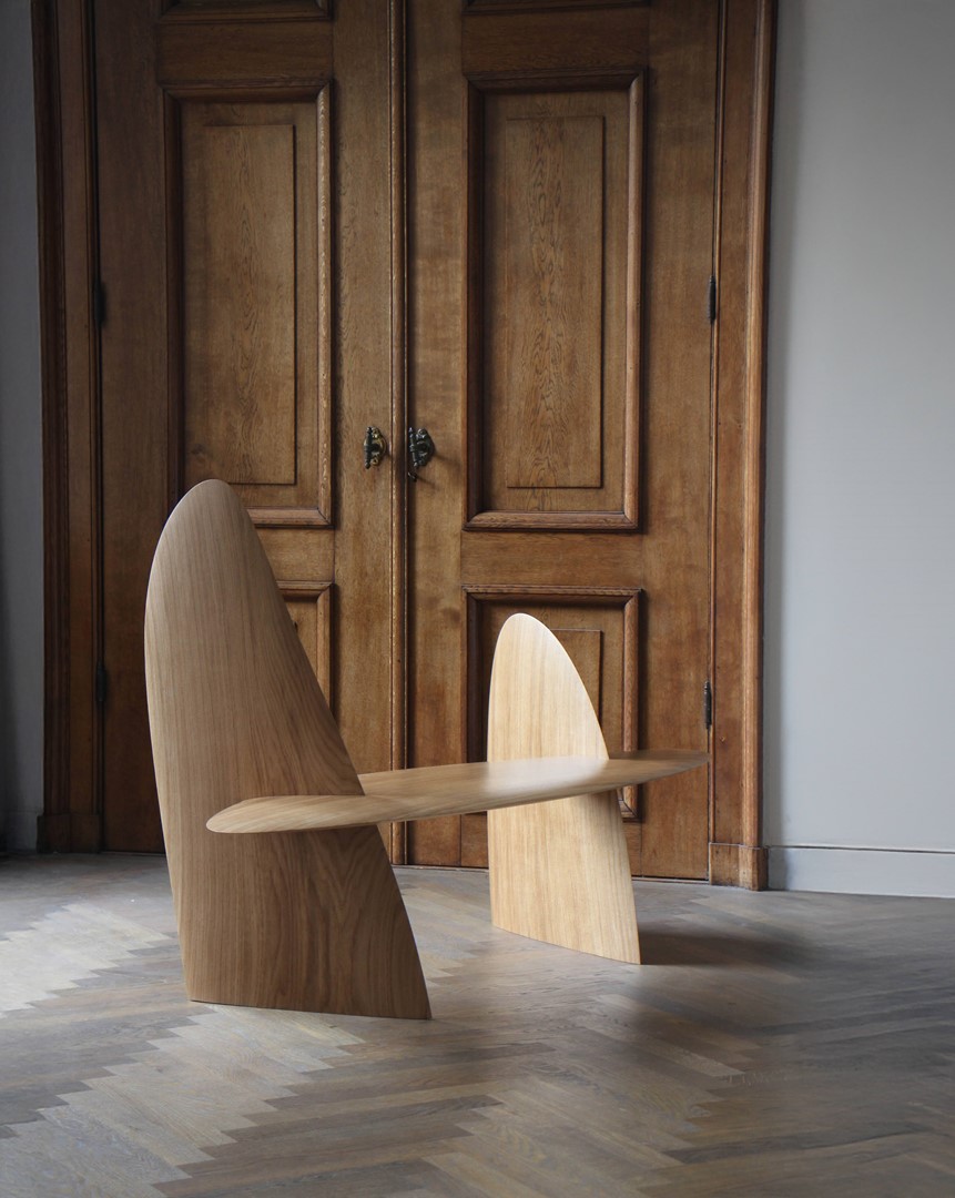 Eikenhouten sculpturale bank van Arne Kristian met vloeiende, asymmetrische vormen, geplaatst voor klassieke houten paneeldeuren op een visgraatvloer.