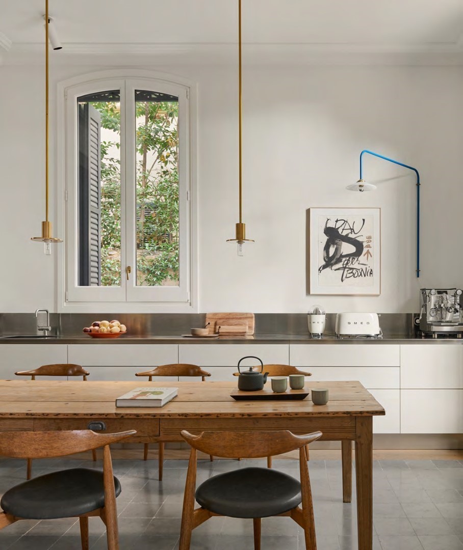 Keuken van Casa Portabella in Barcelona met een grote houten eettafel, zwarte designstoelen, ingebouwde houten kastenwand en veel daglicht via glazen deuren naar de tuin.