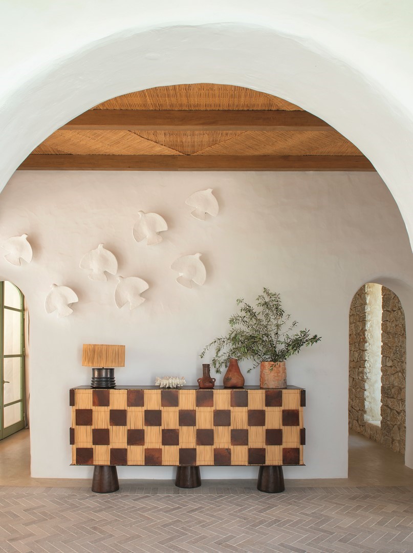 Mediterraan interieur met wit gestucte muur, handgemaakte vogelreliëfs, houten balkenplafond en een vintage dressoir met keramiek en olijftakken in Dar Pichou, Tunesië