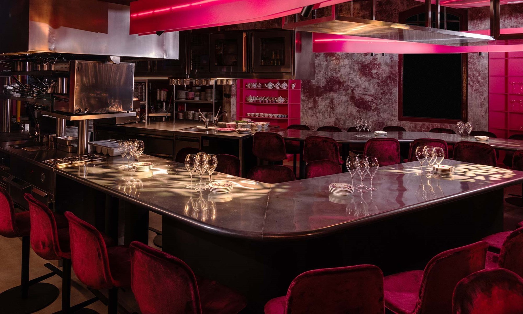 Open restaurantkeuken van Wine Freaks met roze verlichting, verweerde muren en bordeauxrode fluwelen barkrukken, ontworpen door het architectenbureau van Sabrina.