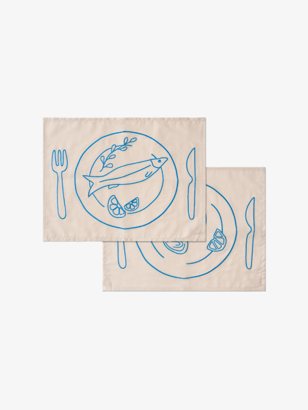 Set van twee beige placemats van Kulu Club met blauw geborduurde visborden, bestek en citroen
