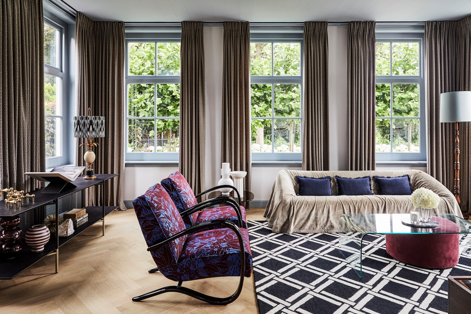 Met royale stoffering werd de akoestiek in huis verbeterd. Hier in de woonkamer met een vloerkleed van Nourison en gordijnen Balmoral van Casamance met subtiele pailletten. De bank Mantilla is van Kazuhide Takahama via Morentz, de fauteuils zijn vintage.