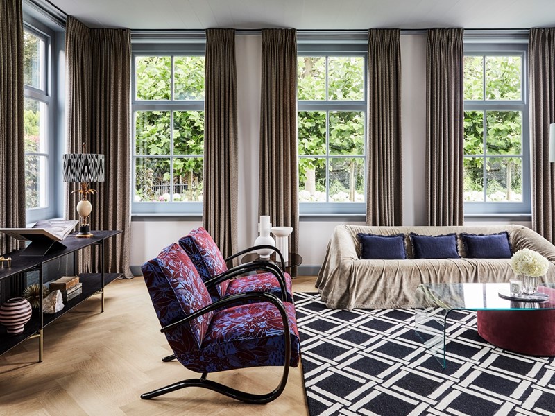 Met royale stoffering werd de akoestiek in huis verbeterd. Hier in de woonkamer met een vloerkleed van Nourison en gordijnen Balmoral van Casamance met subtiele pailletten. De bank Mantilla is van Kazuhide Takahama via Morentz, de fauteuils zijn vintage.