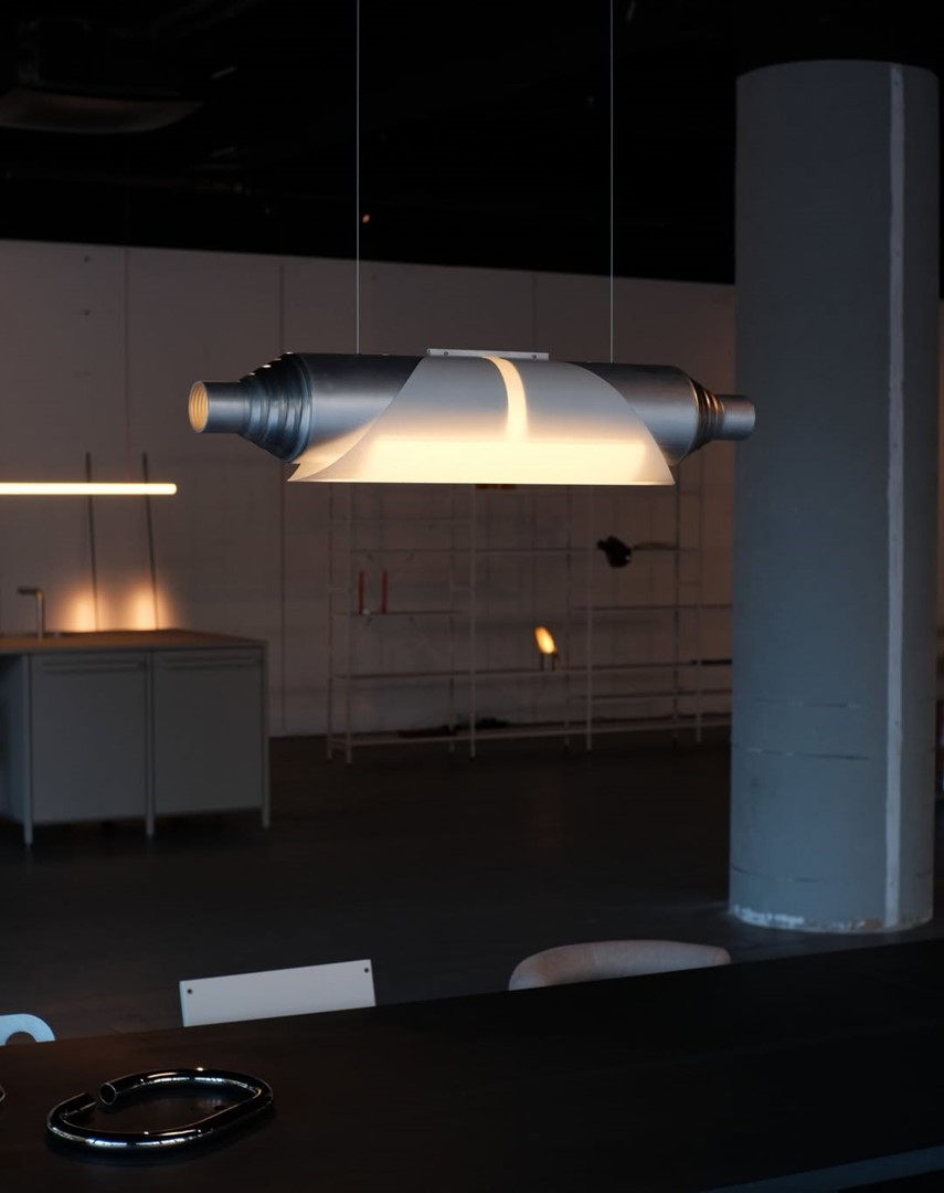 Hanglamp van opengefreesde aluminium buis, omwikkeld met washipapier, zwevend boven een donkere tafel in een industriële ruimte; ontwerp Zowa Rindt.