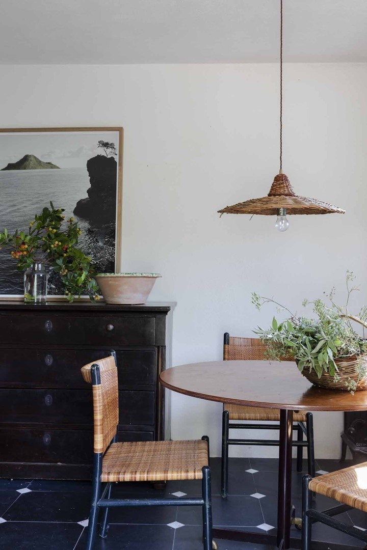 ethoek in gastenhuis met rotan stoelen, antieke ladekast en rieten hanglamp op zwart-wit tegelvloer, mediterraans interieur Ligurië