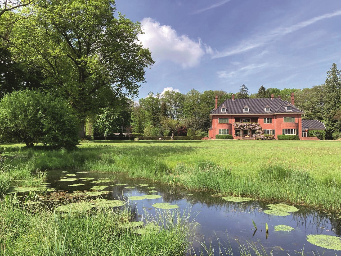 Groengrasveld met vrijstaande woning met orde bakstenen  en sloot.