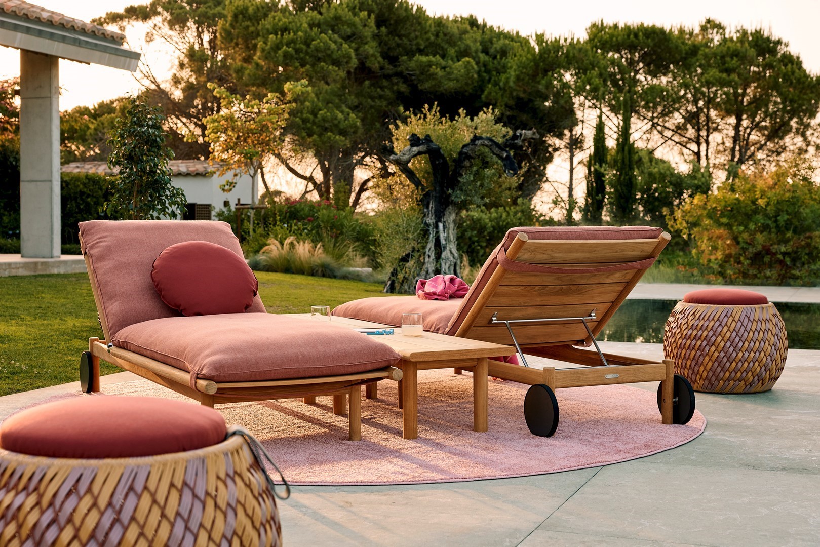 Terras inrichten met teakhouten ligbedden en roze kussens naast een zwembad