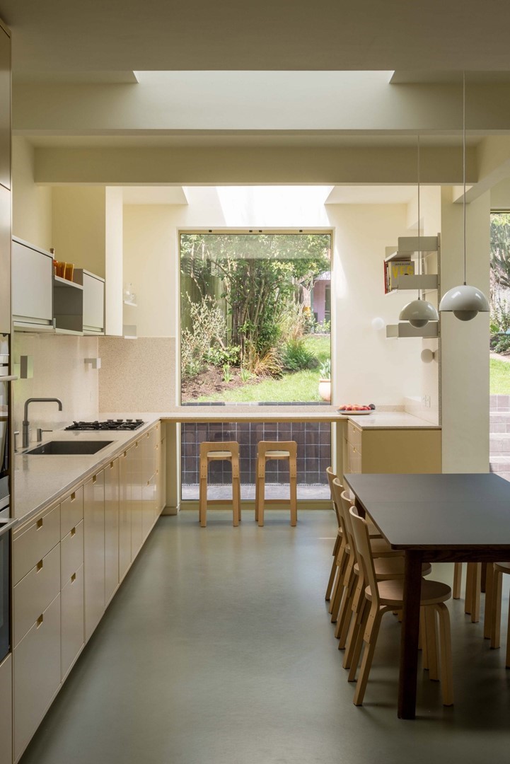 Lichte keuken met ingebouwde lichtkoepels en uitzicht op een groene tuin, ingericht met houten barkrukken en een moderne eettafel met stoelen.