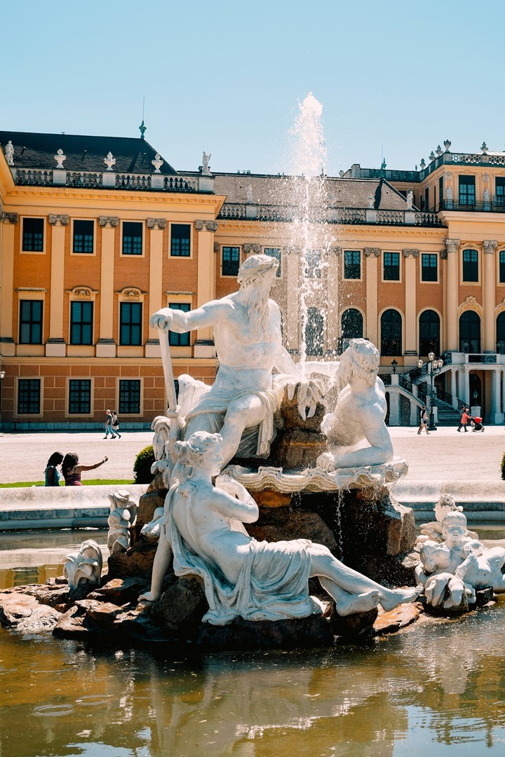 Fontein met klassieke beelden bij Schloss Schönbrunn in Wenen met barok paleis op de achtergrond