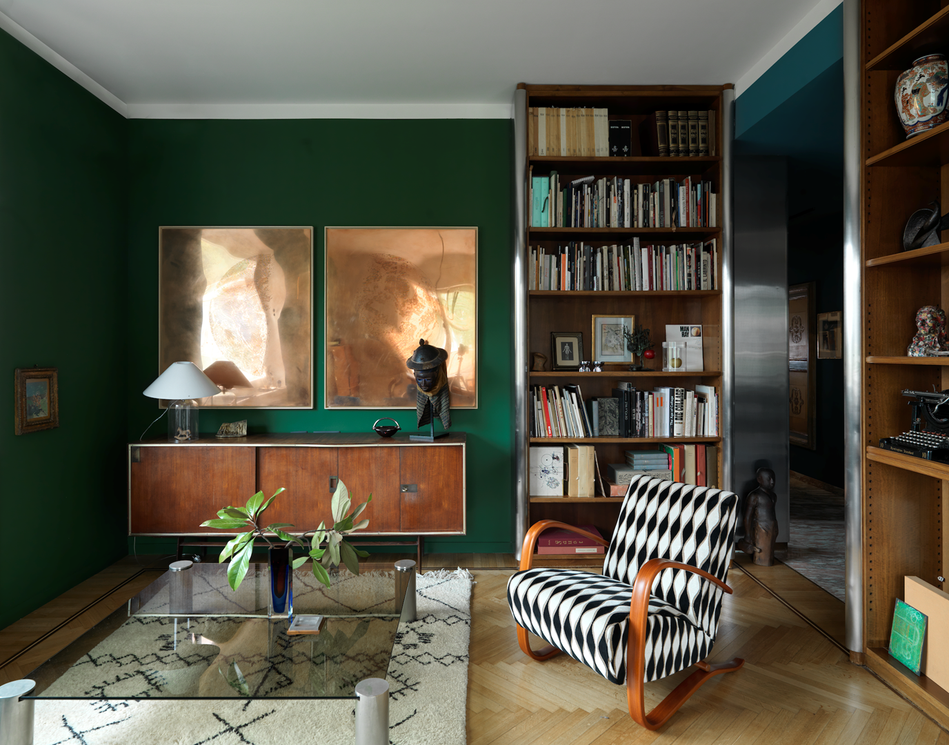 De bosgroen geschilderde woonkamer vroeg om kunstwerken rond het thema natuur. Aan de muur een tweeluik van koperen platen met de maan erin gegraveerd: Crepuscolo (2019) van Marco De Sanctis. Op het vintage dressoir staat een Yoruba-masker uit Nigeria. Leeslamp Alega links is van Vico Magistretti voor Vistosi.