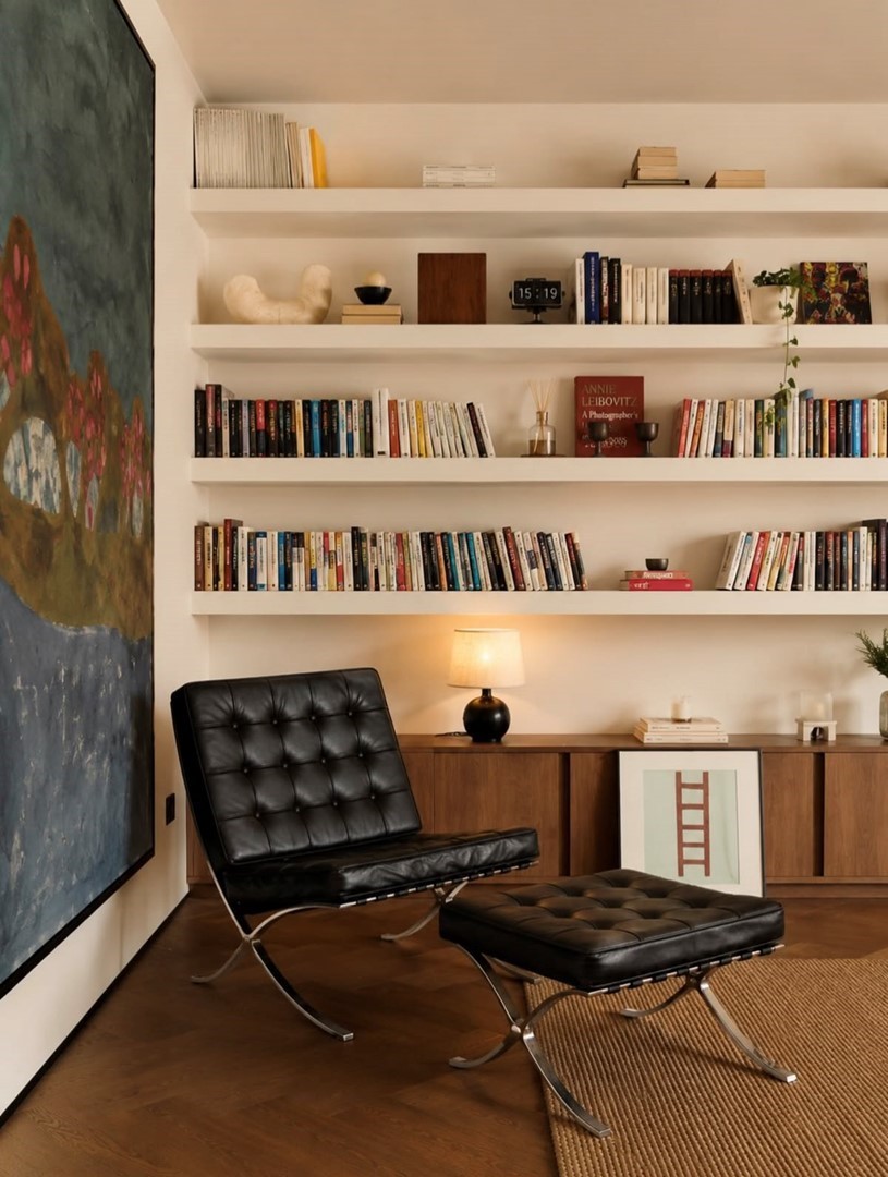 Leeshoek met ingebouwde boekenplanken, een zwarte Barcelona-fauteuil en een schilderij van een waterlelievijver.