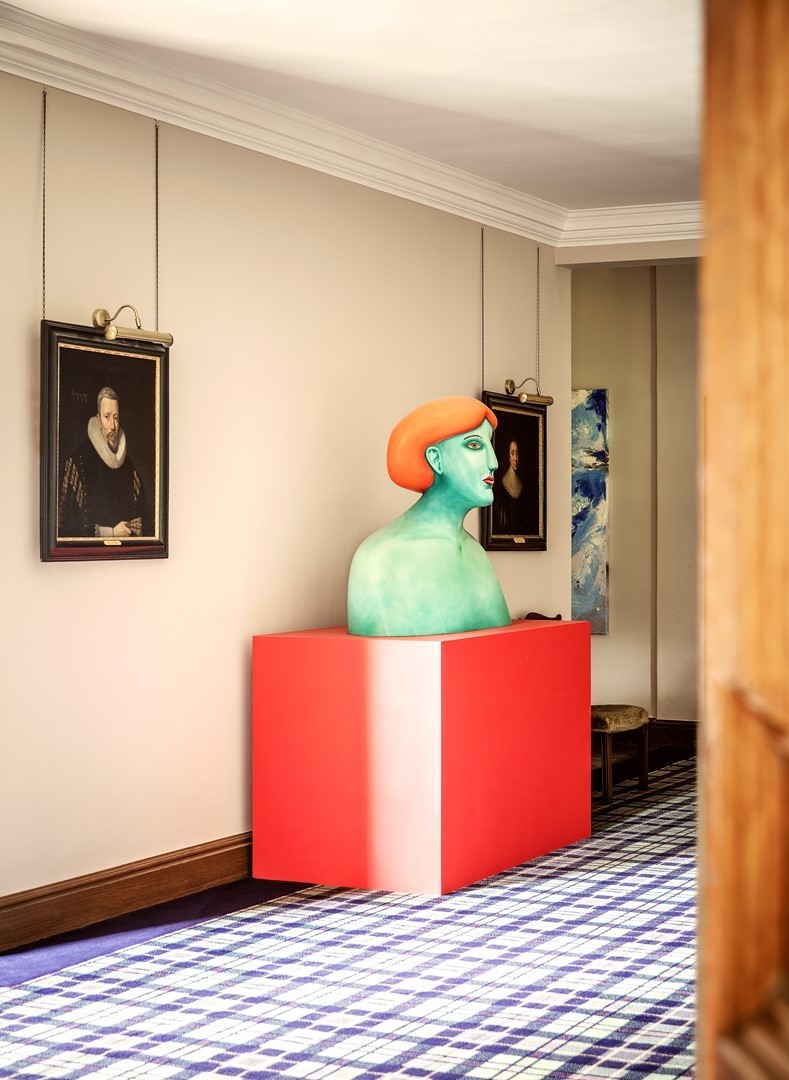 Turquoise buste met oranje haar op een rode sokkel, tussen klassieke portretten in een gang van Cortachy Castle