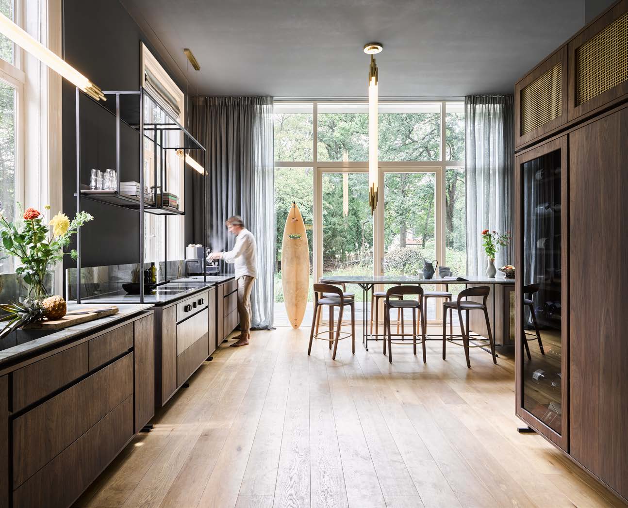 De modulaire keuken, een eigen ontwerp gemaakt door Koen Vleugel, is uitgevoerd in notenhout en staal met een marmeren werkblad. De hanglampen zijn van DCW Éditions, de barkrukken van Artisan en de gordijnen van Étoffe Unique. (Foto: Alexander van Berge).