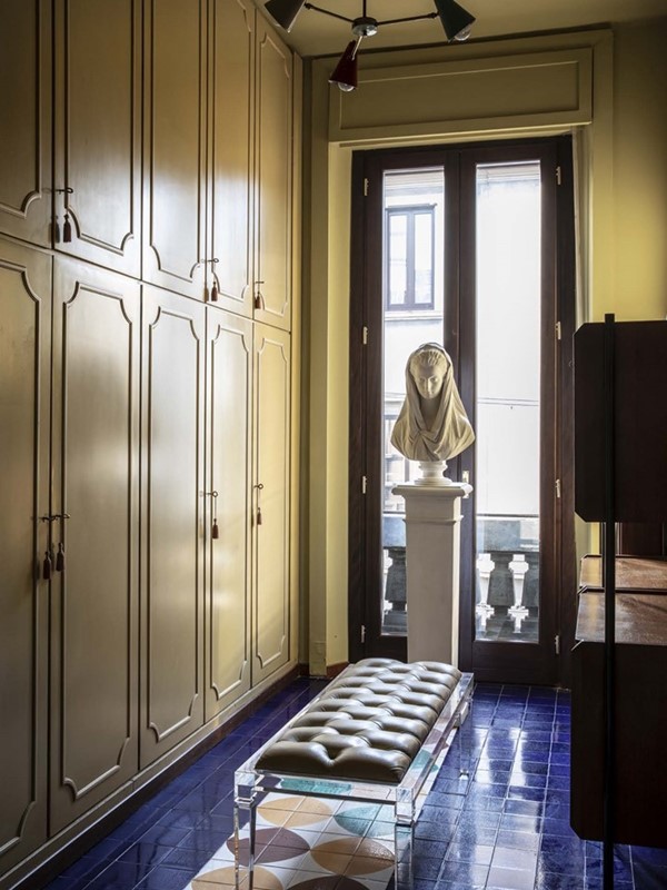 De walk-in closet met originele tegelvloer van Bobo Piccoli. Het centrale bankje van perspex is vintage en werd geproduceerd door Fabian Art. De jaren vijftig modulaire kast tegen de rechterwand werd geproduceerd door Fratelli Dassi. De plafondlamp is een ontwerp uit de jaren vijftig voor Stilnovo. De buste uit gips werd gemaakt door Fumagalli & Dossi.